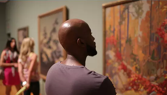 Des personnes contemplent des tableaux accrochés au mur
